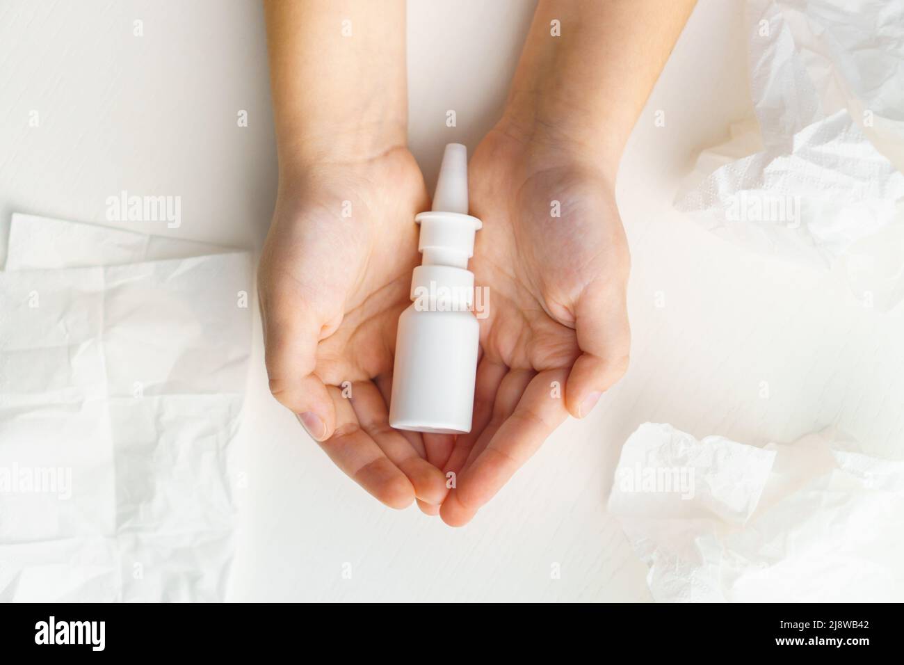 Child hands hold bottle nose spray on white background with paper tissue. Runny nose treatment Stock Photo