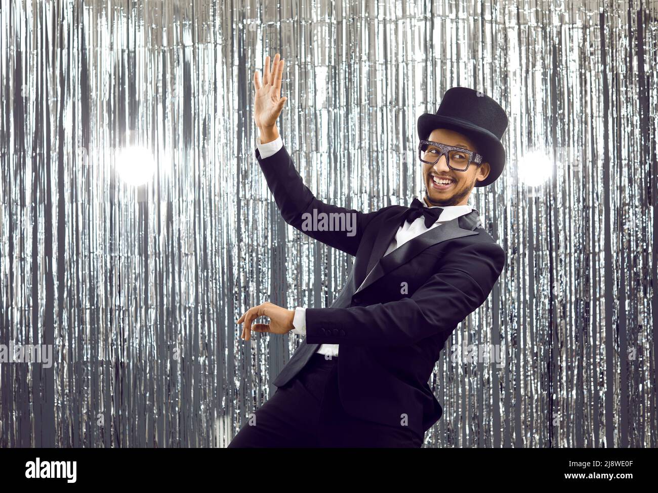 Happy funny young black man in suit, bow tie and top hat dancing and having fun at party Stock Photo
