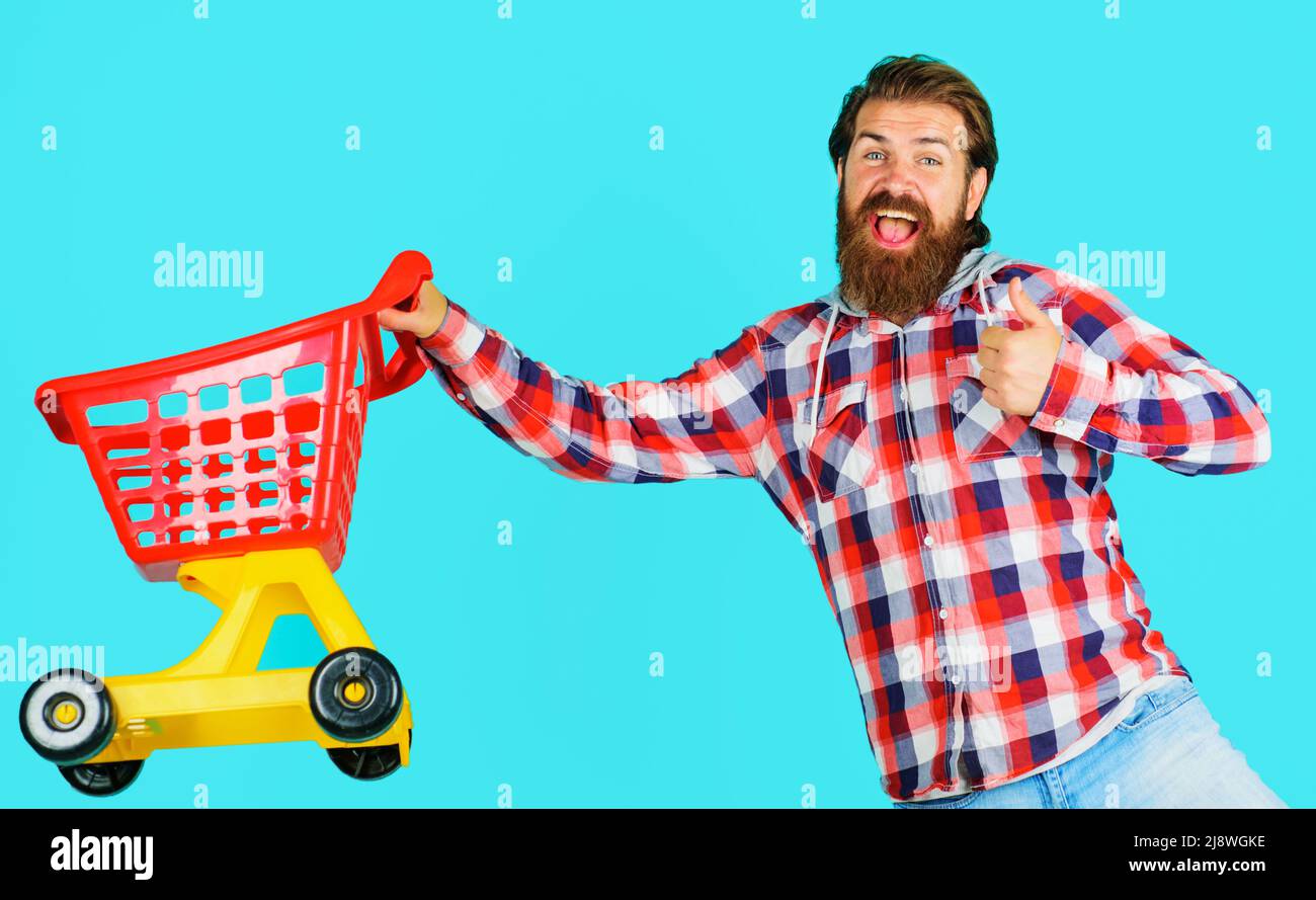 Happy bearded man with empty shopping trolley shows thumb up. Buyer in supermarket. Sale. Discount. Stock Photo