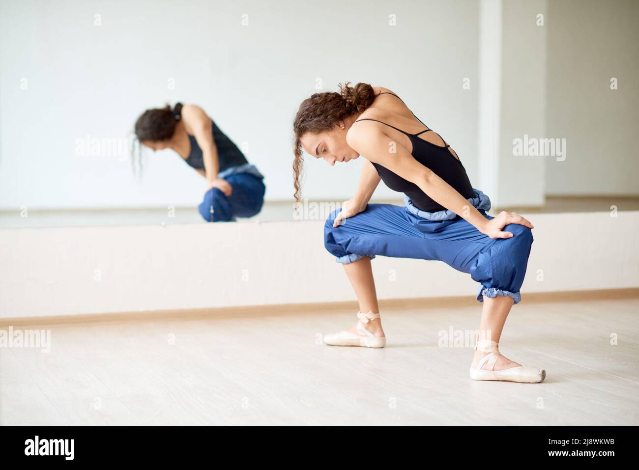 Young female ballet dancer stretching her body before rehearsal in dancing hall Stock Photo