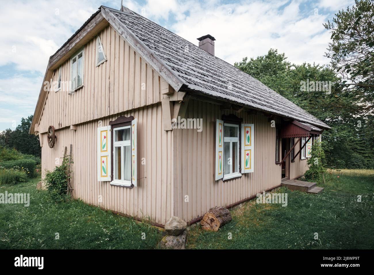 Old traditional wooden house with windows and shutters, rear view. An old carriage wheel is hung on the wall, the roof is covered with wooden tiles. Stock Photo