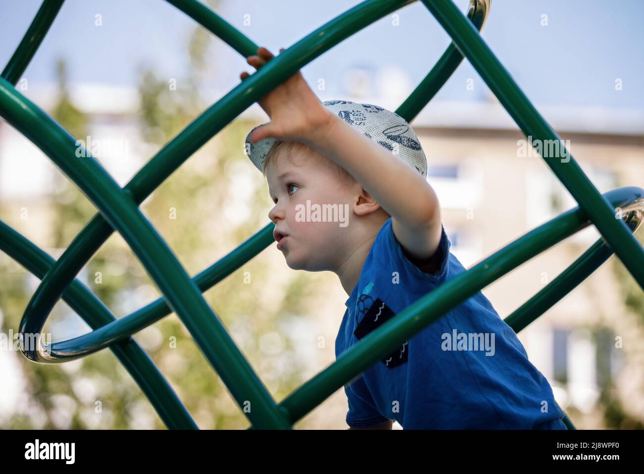 Little boy very focused climb on the green tube ladders in playground. Stock Photo