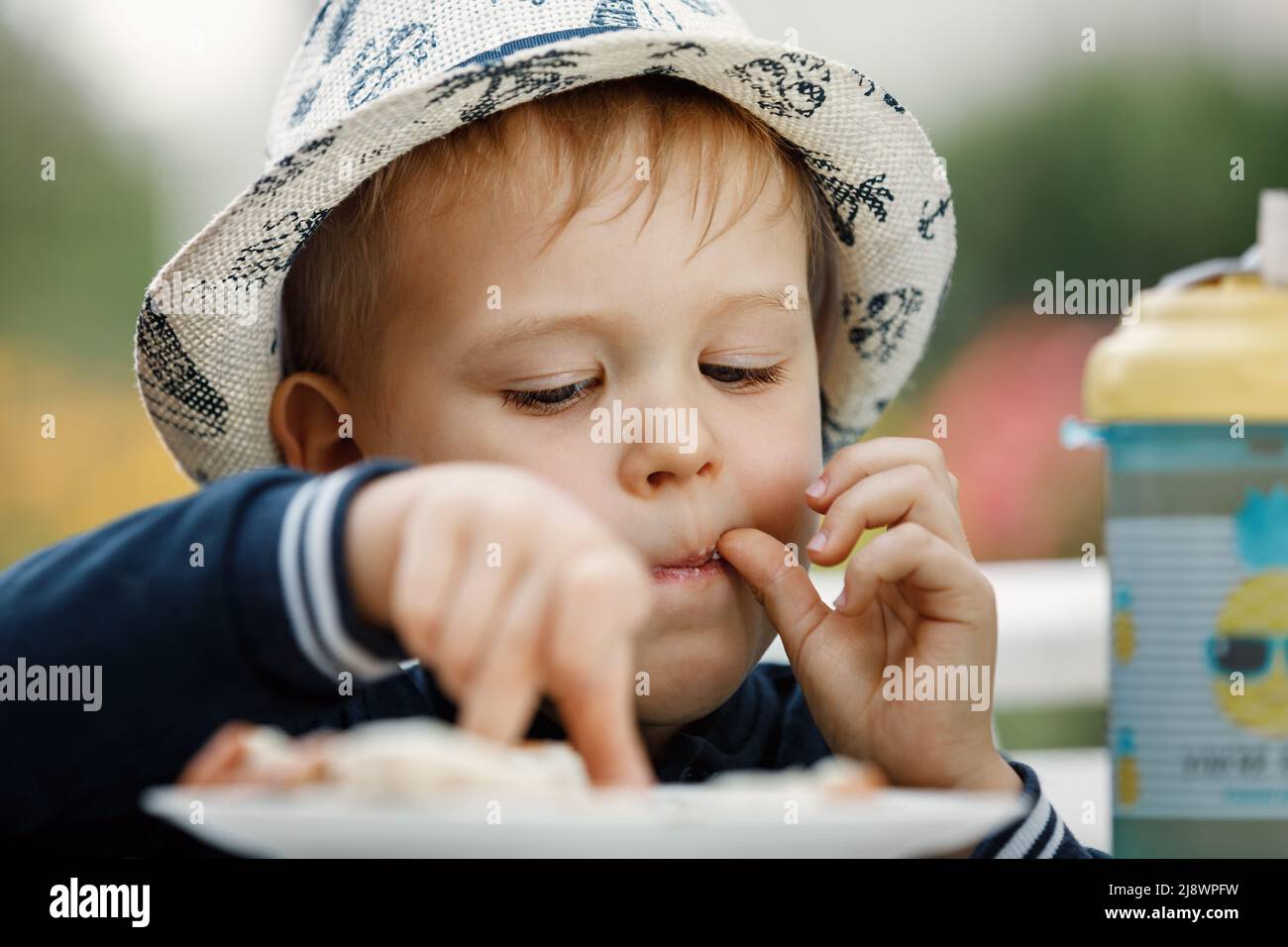 The boy in the summer garden chooses and tastes food from a plate. Stock Photo