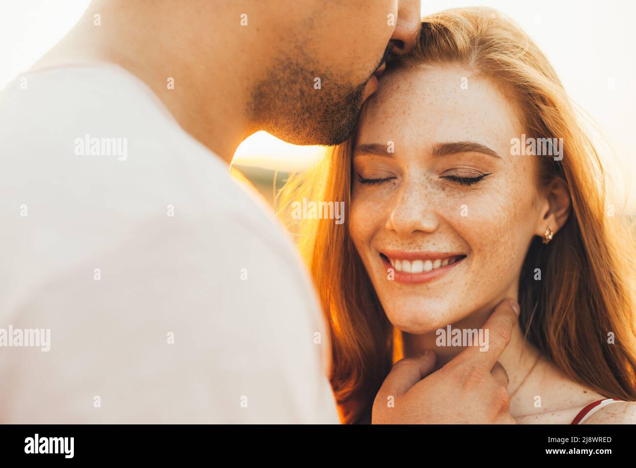 The freckled girl smiling with her eyes closed while her boyfriend kisses her on the forehead