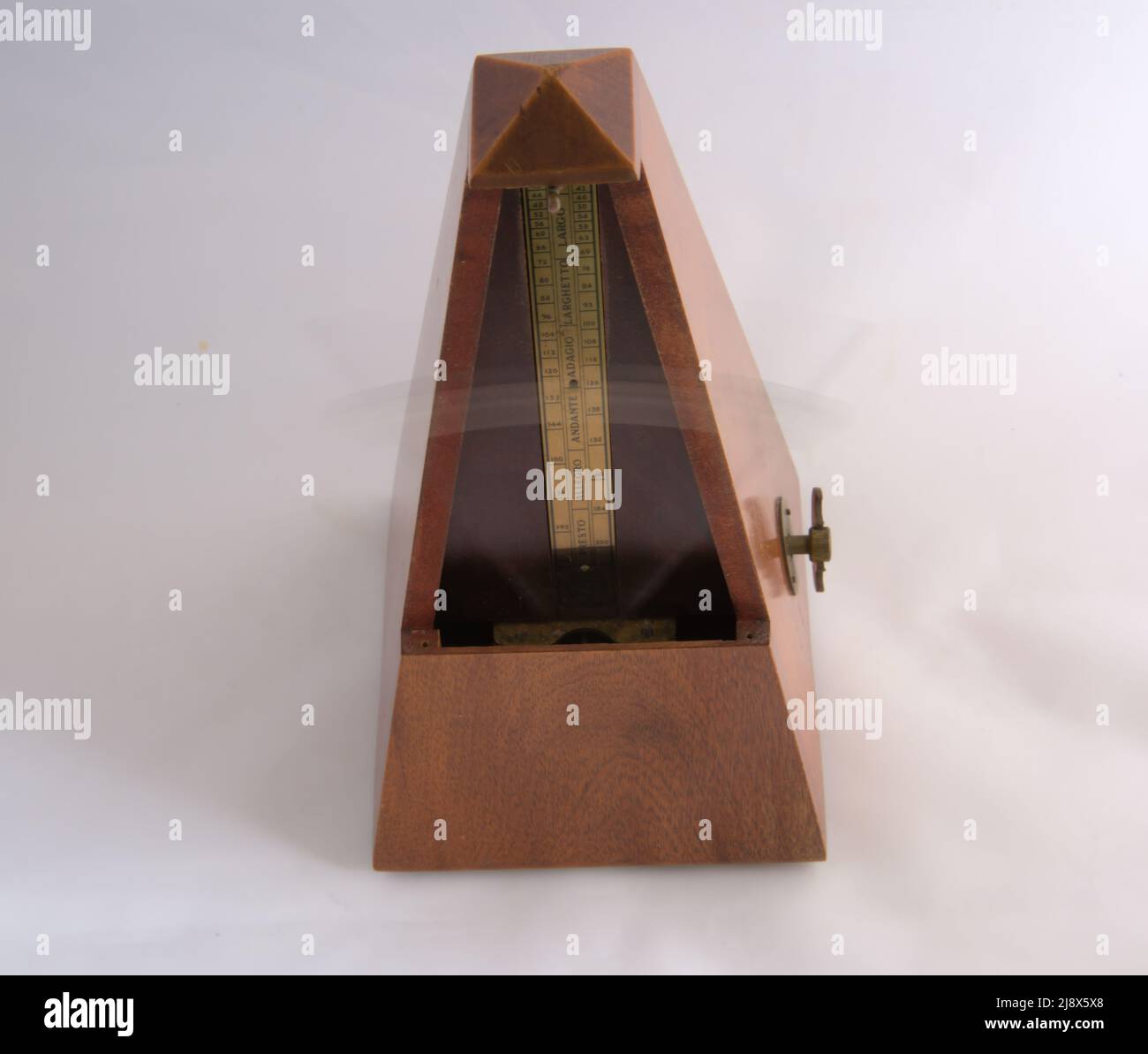 Old metronome witth pendulum swinging.and winding mechanism on the side. Stock Photo