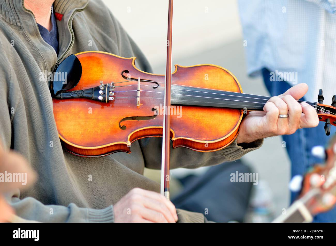 Musicisan plays a fiddle at an outdoor festival,  using a bow and changing tones with fingers on the strings. Stock Photo