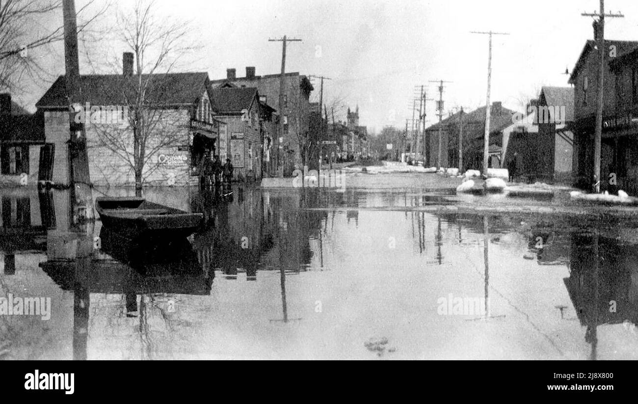 A boat tied to a lamppost on Bridge Street West, close to Everett Street in Belleville, Ontario, during the 1918 floods. The Kellaway general store is on the left.  The tower of Bridge Street Methodist Church is in the background  ca.  1918 Stock Photo