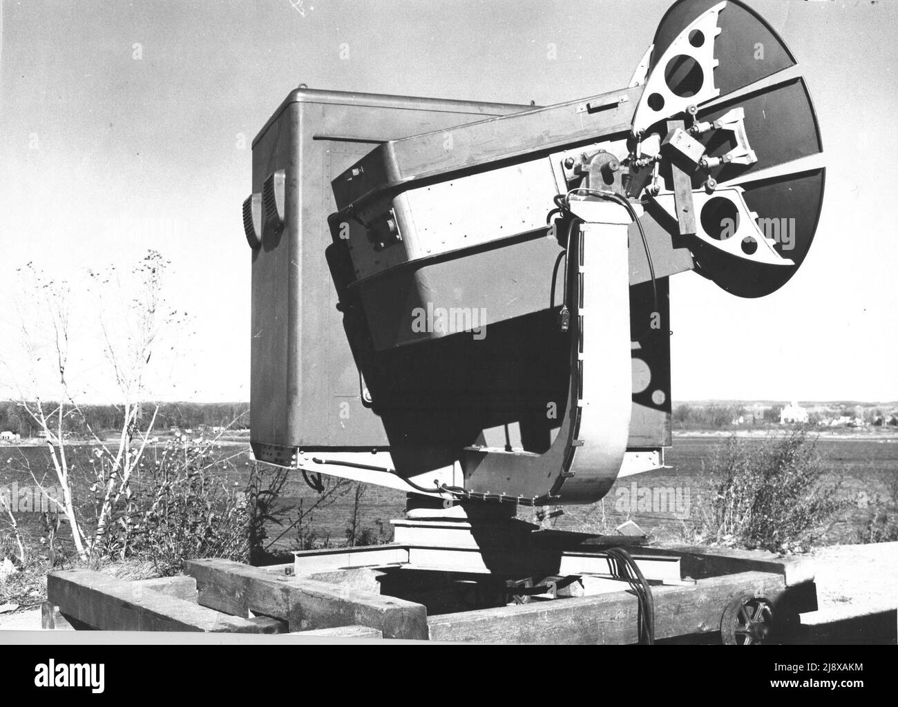 The National Research Council of Canada developed this unique version of a Searchlight Control Radar between 1942 and March 1944. It did not guide a searchlight directly like its British counterparts. Instead, an operator in the cabin could verify the target the radar was tracking through a window (not visible here) and the signals would be sent to a searchlight to aim it. During testing, it was found that the system could track so rapidly that the operators had motion sickness and development was abandoned.  ca.   1943 - 1944 Stock Photo