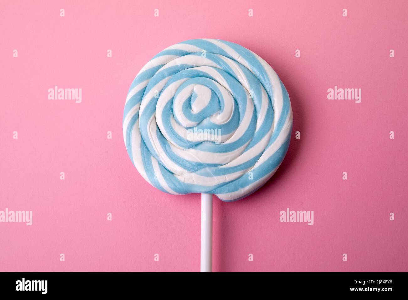 Blue lollipop on a pink background. Sweets, party and unhealthy food