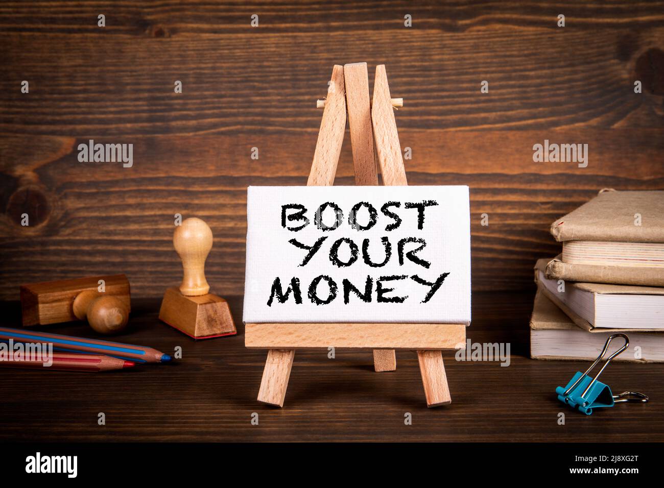 BOOST YOUR MONEY. Miniature easel on a wooden office desk. Stock Photo