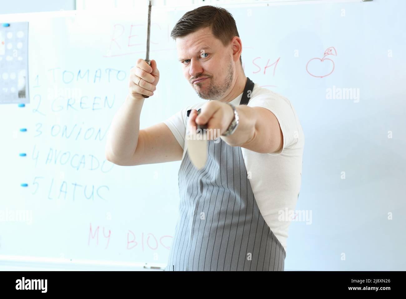 Standing man hold sharp kitchenware for cooking, knife sharpening on kitchen Stock Photo