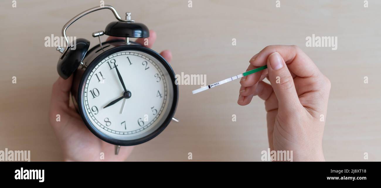 Woman holds a positive pregnancy test and alarm clock. Nine months of