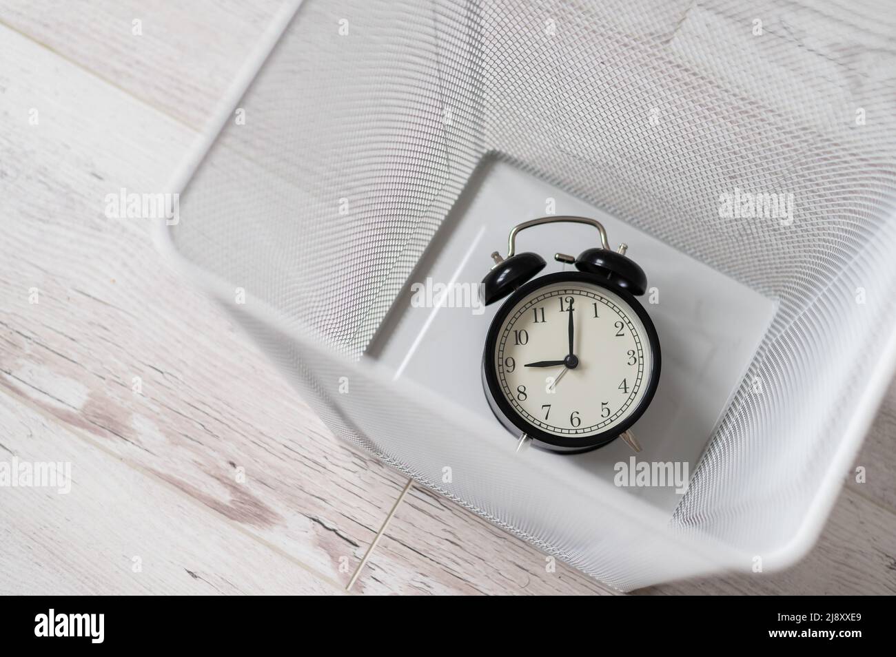 Top view of an alarm clock discarded in a white mesh metal trash bin. The concept of wasted time. Stock Photo
