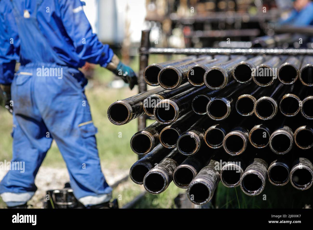 Oil rig drill pipes stacked with oil industry workers in the background