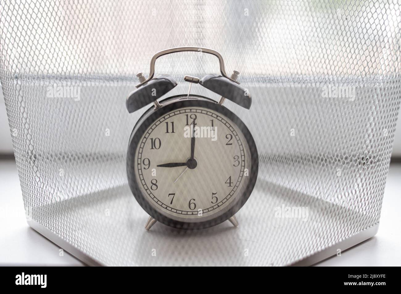 alarm clock discarded in a white mesh metal bin. The concept of wasted time. Stock Photo