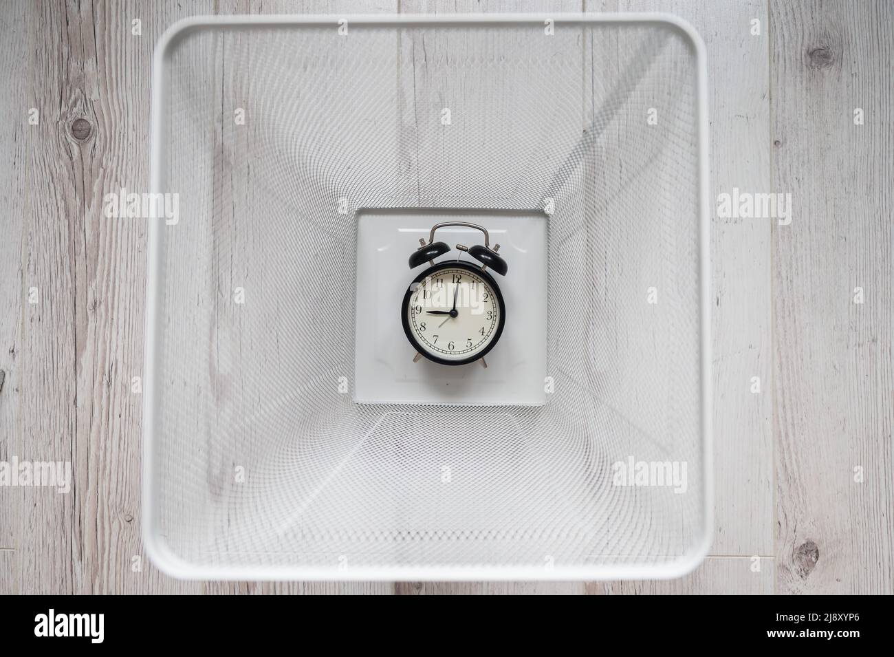 Top view of an alarm clock discarded in a white mesh metal trash bin. The concept of wasted time. Stock Photo