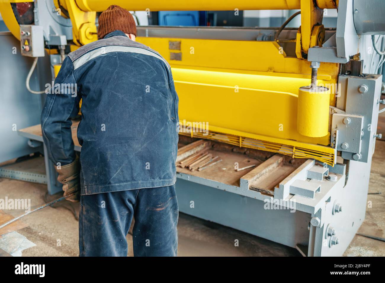 Worker cuts metal on mechanical guillotine machine in production hall. Industrial equipment for metal cutting. Real scene. Real workflow. Man at work. Stock Photo