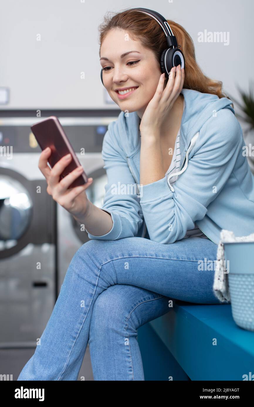happy young woman using her phone while doing laundry Stock Photo