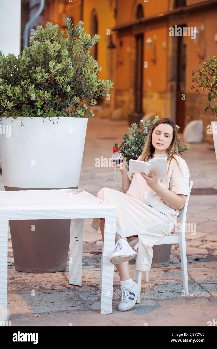 https://c8.alamy.com/comp/2J8YDW5/vertical-elegant-and-charming-blond-woman-read-book-and-drink-alcohol-sit-at-table-in-cafe-learn-language-travelling-2J8YDW5.jpg