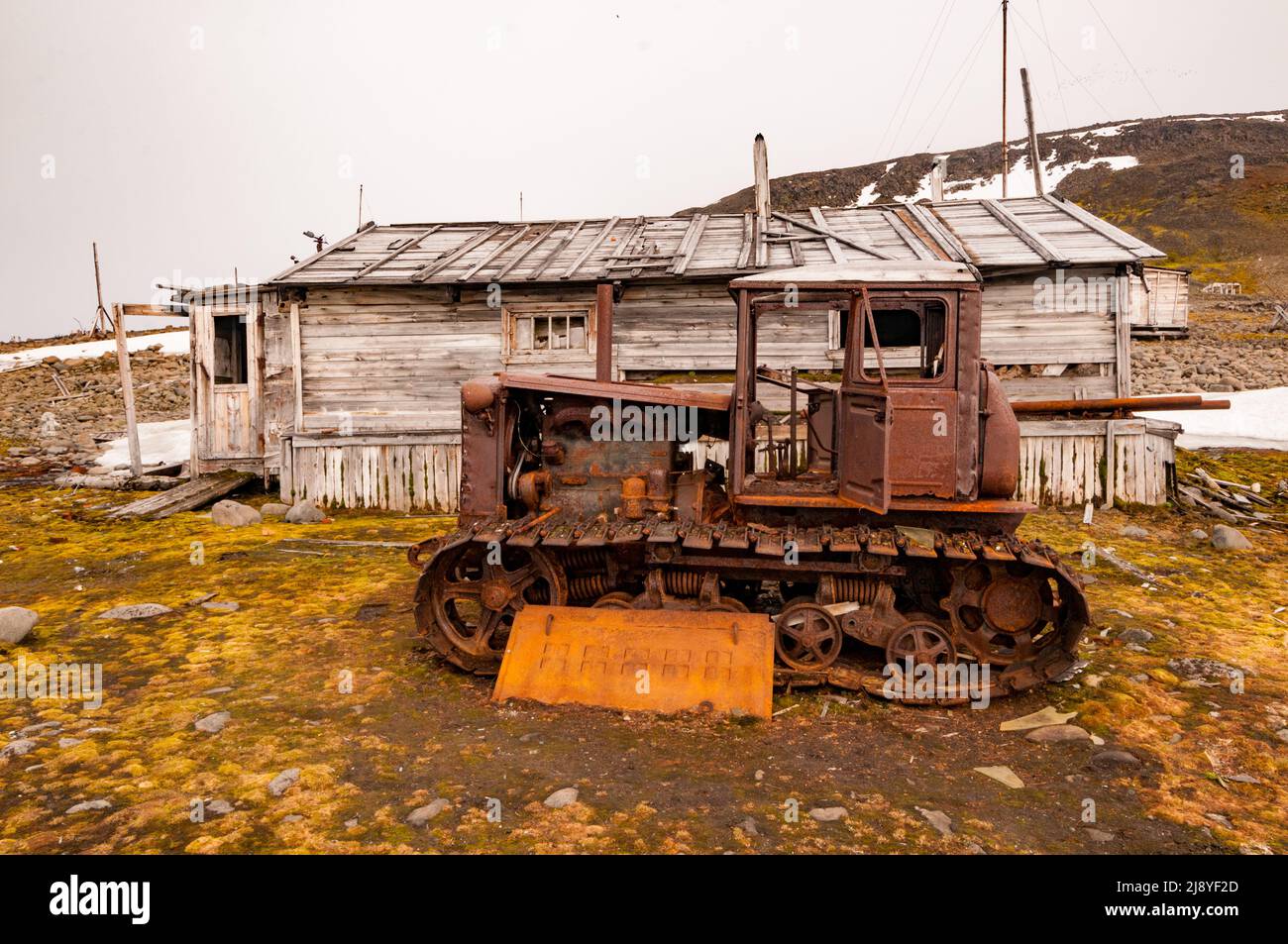 An abandoned, rusting vehicle with caterpillar tracks, outside a dilapidated hut at the abandoned research station on Bukhta Tikhaya, Franz Josef Land Stock Photo