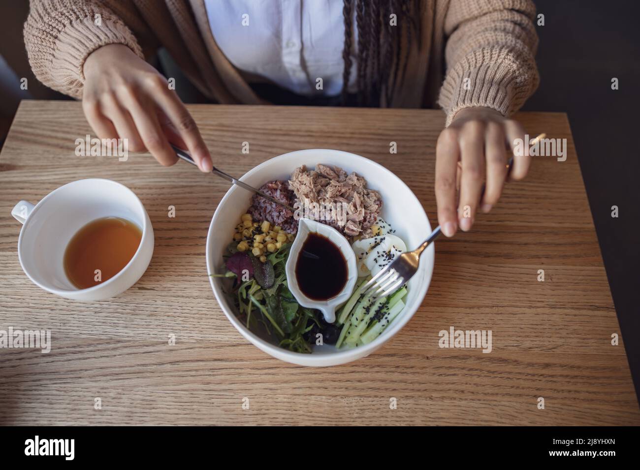 Top view to female hands holding fork and knife and eating delicious healthy food served in a white ceramic bowl Stock Photo