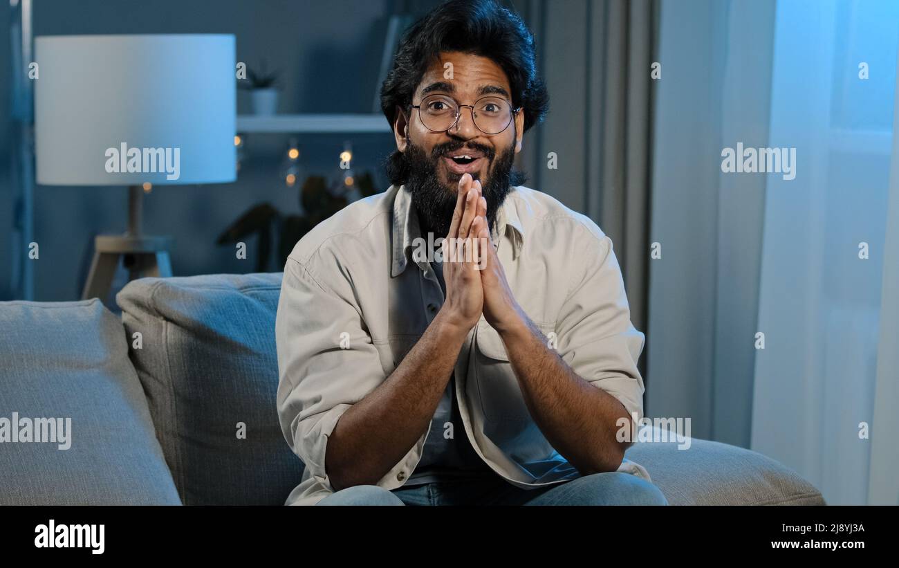 Arabic happy motivated man watching TV at home at night late in evening. Spaniard bearded Indian guy millennial male fan of favorite sports team rejoi Stock Photo