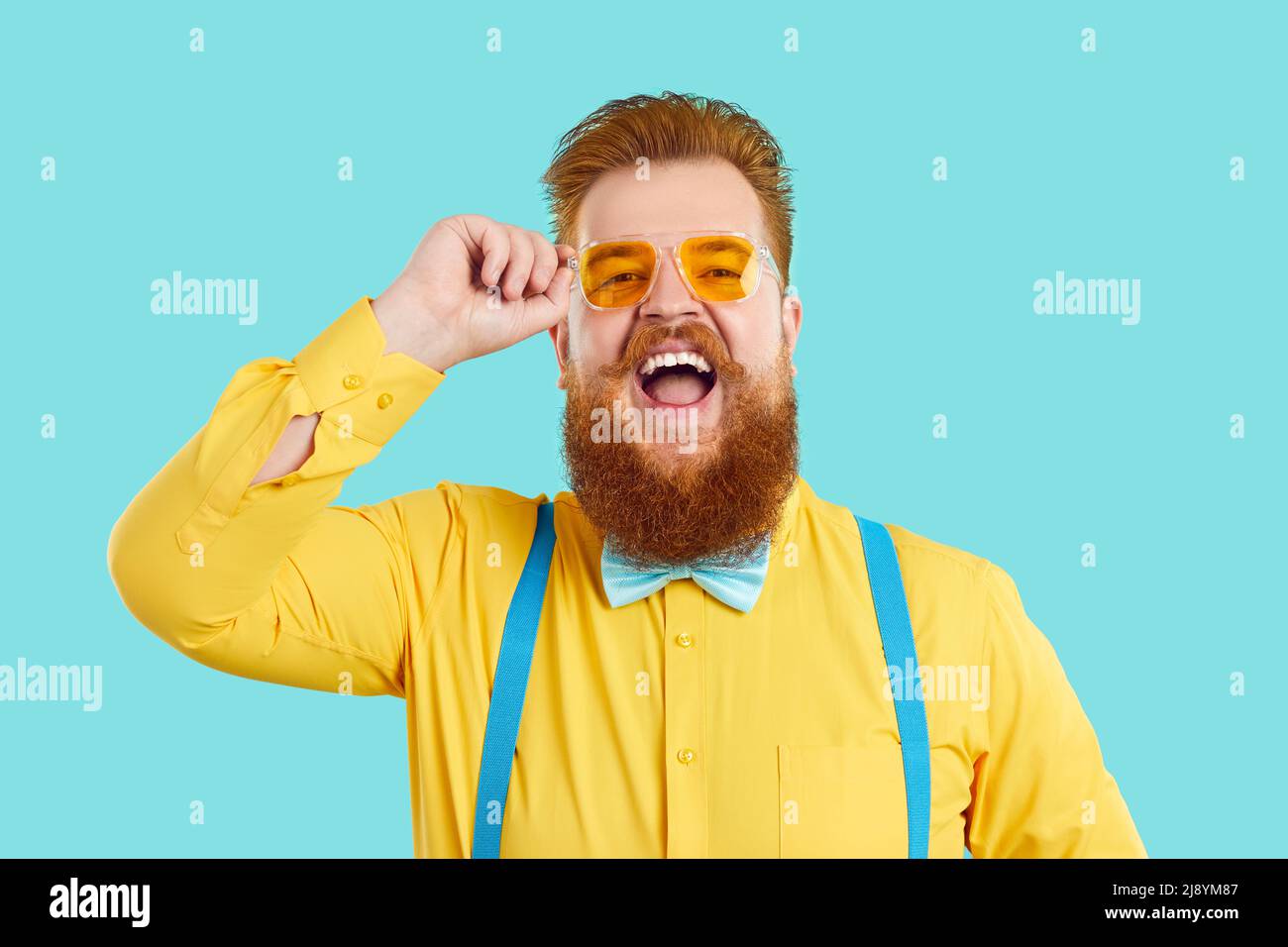 Cheerful stylish chubby man in fashionable glasses laughs out loud on light blue background. Stock Photo