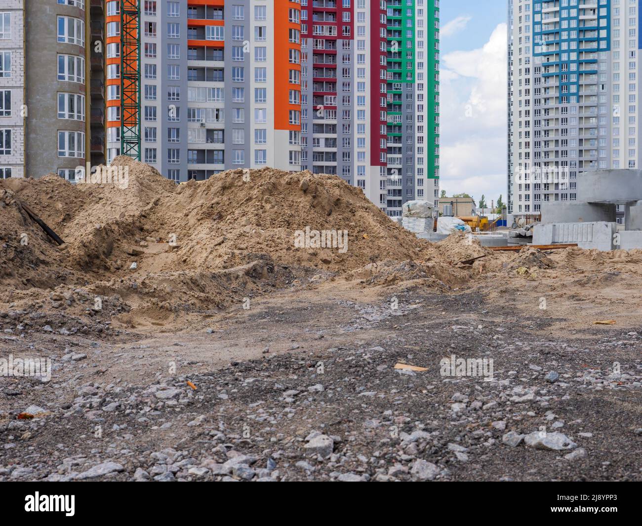 A building site with heaps of sand, concrete rings in the foreground and new colorful high-rise buildings and construction equipment in the background Stock Photo