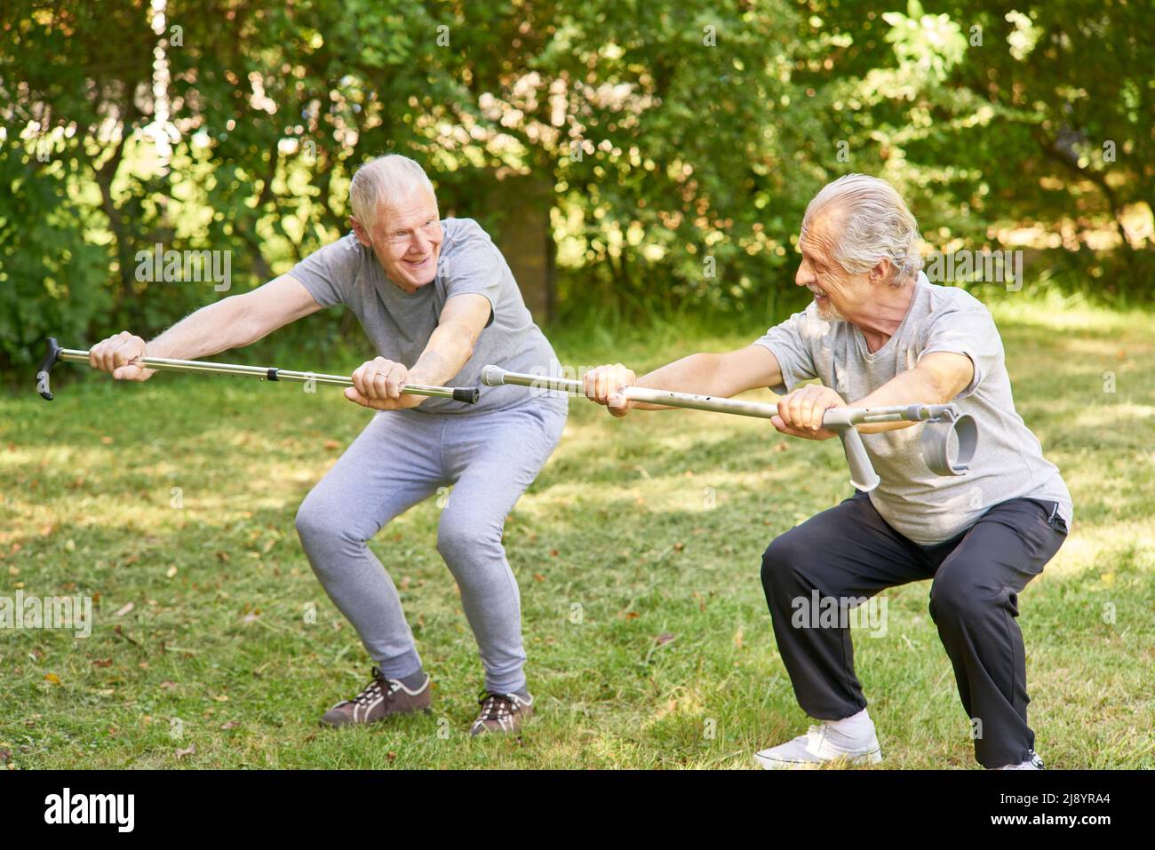 Two seniors do squats with crutches as a sport in the garden Stock