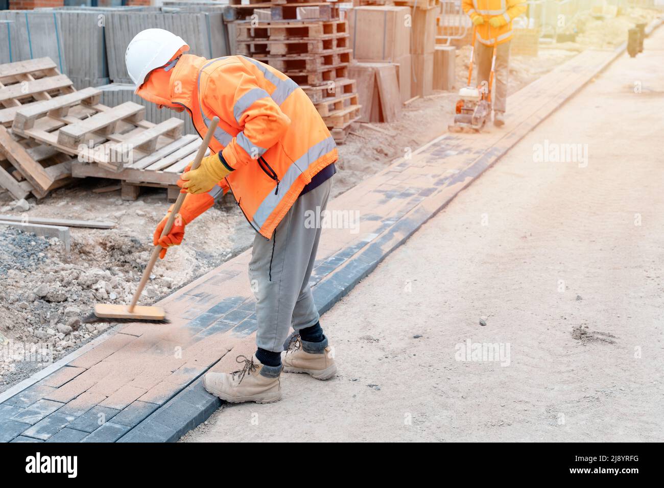 Construction workers filling joints of the block paved footpath with