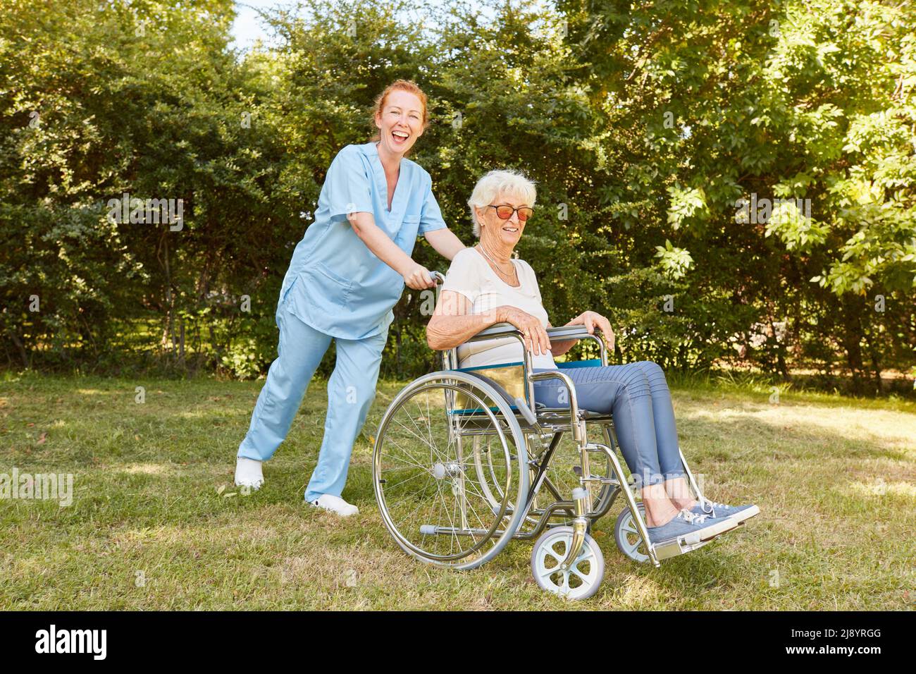 Cheerful geriatric nurse pushes old woman in a wheelchair after a