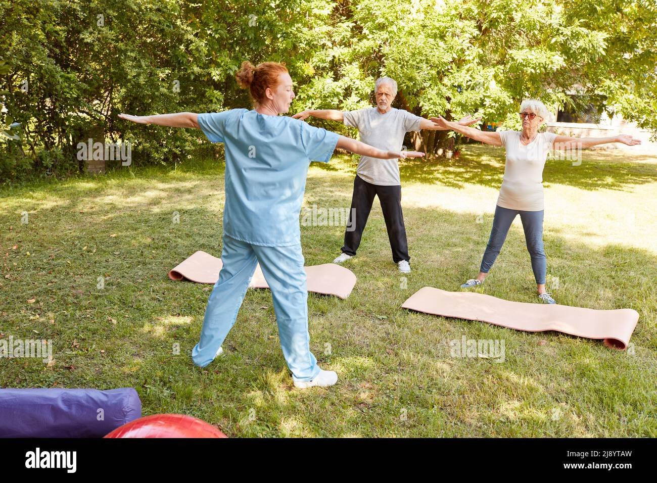 Senior man doing gymnastic rehab exercise with stretched arms with trainer in summer in nature Stock Photo