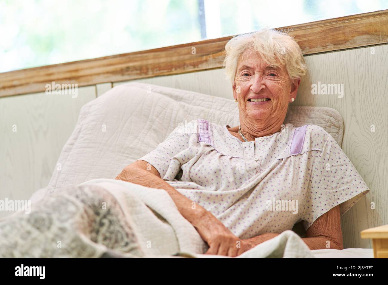 Smiling senior woman as bedridden patient on bed in hospital or nursing
