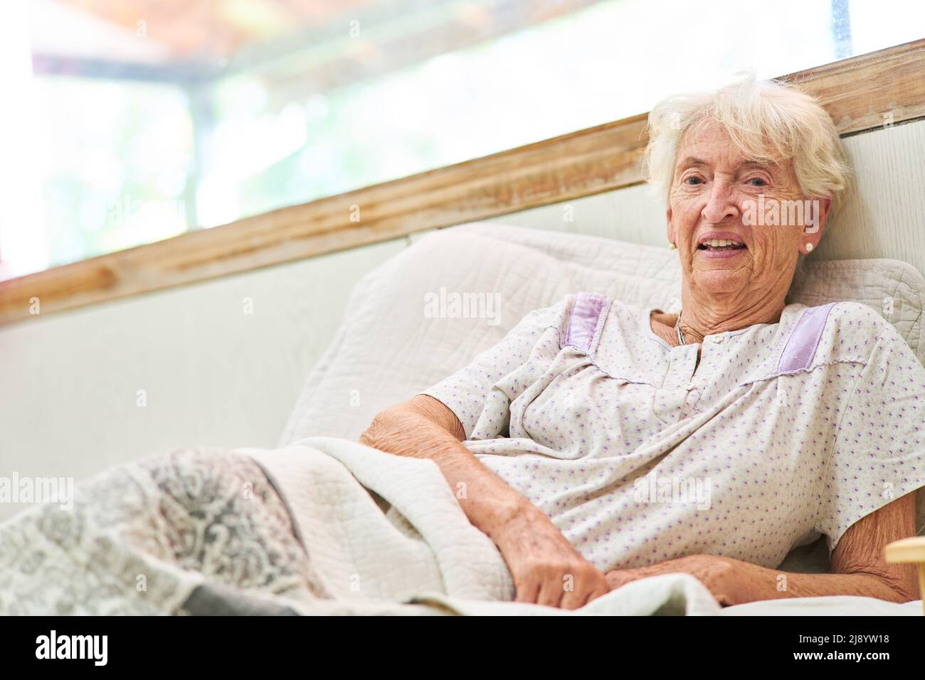 Old sick woman in pajamas as patient lies in bed in hospital or retirement home Stock Photo
