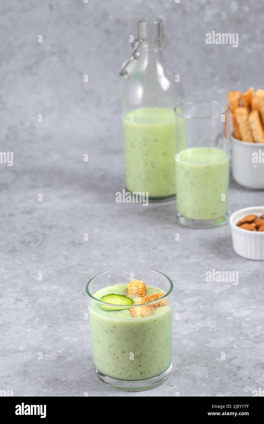 Chilled cucumber soup with nuts, herbs, yogurt, crackers in a glass beaker on a gray background. healthy vegan food Stock Photo