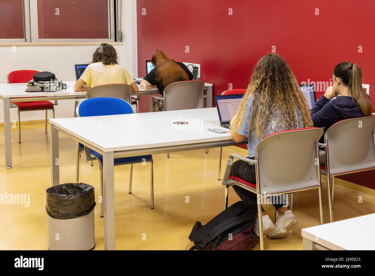 Rear view and Long exposure Photography of Students preparing the exams at night so, one young woman is blurred for her head movement Stock Photo