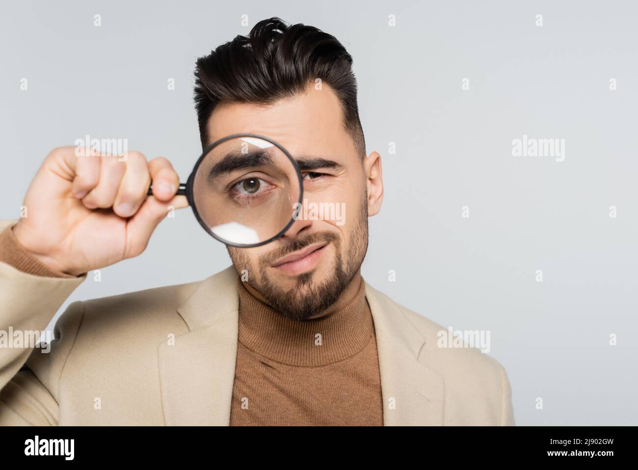 picky critic looking at camera through magnifying glass isolated on grey Stock Photo
