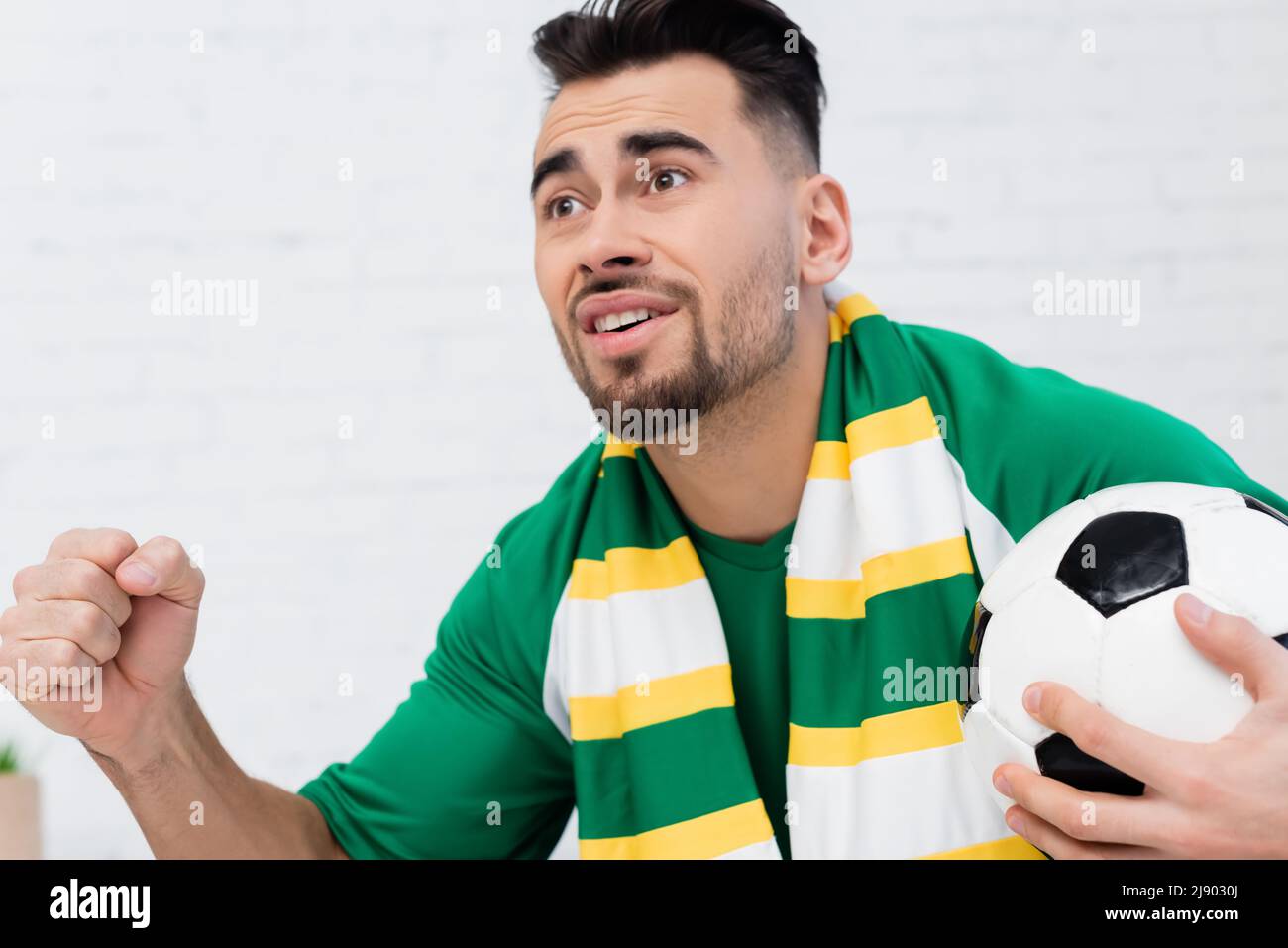 excited sports fan holding soccer ball and clenched fist for luck while
