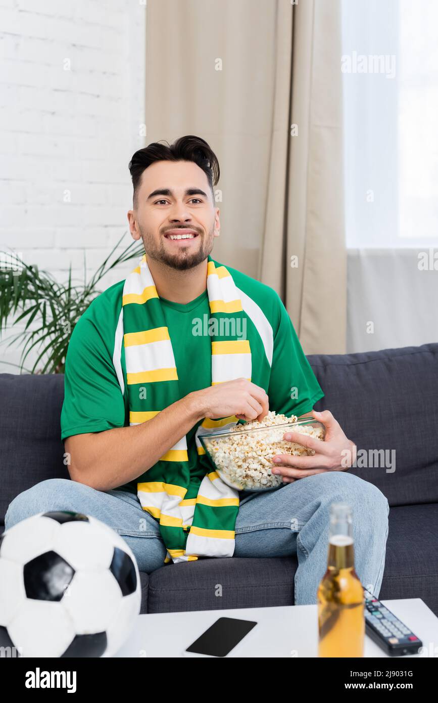 happy football fan with bowl of popcorn watching match on tv at home