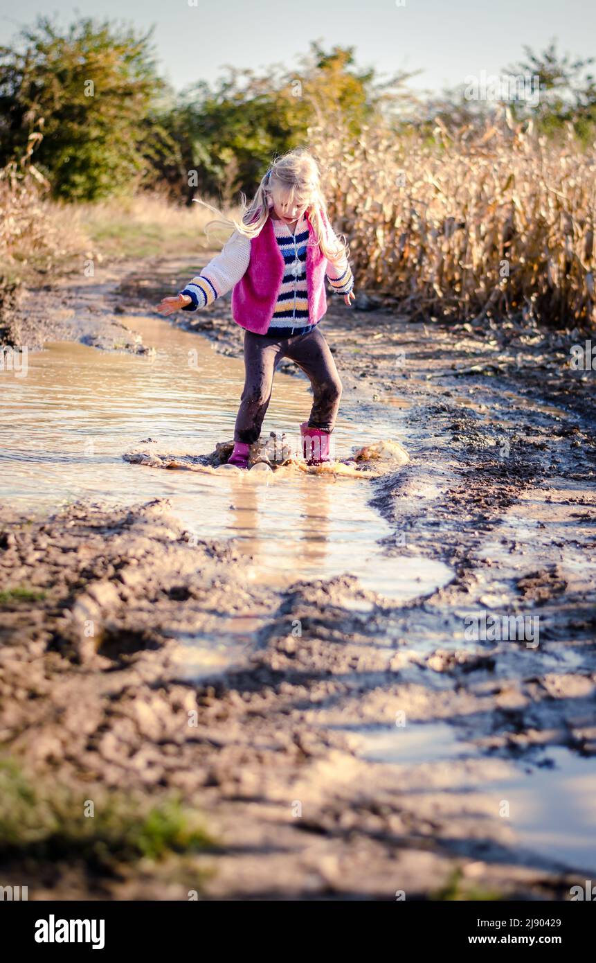 little lovely girl enjoying water puddle after rain in seasonal ...