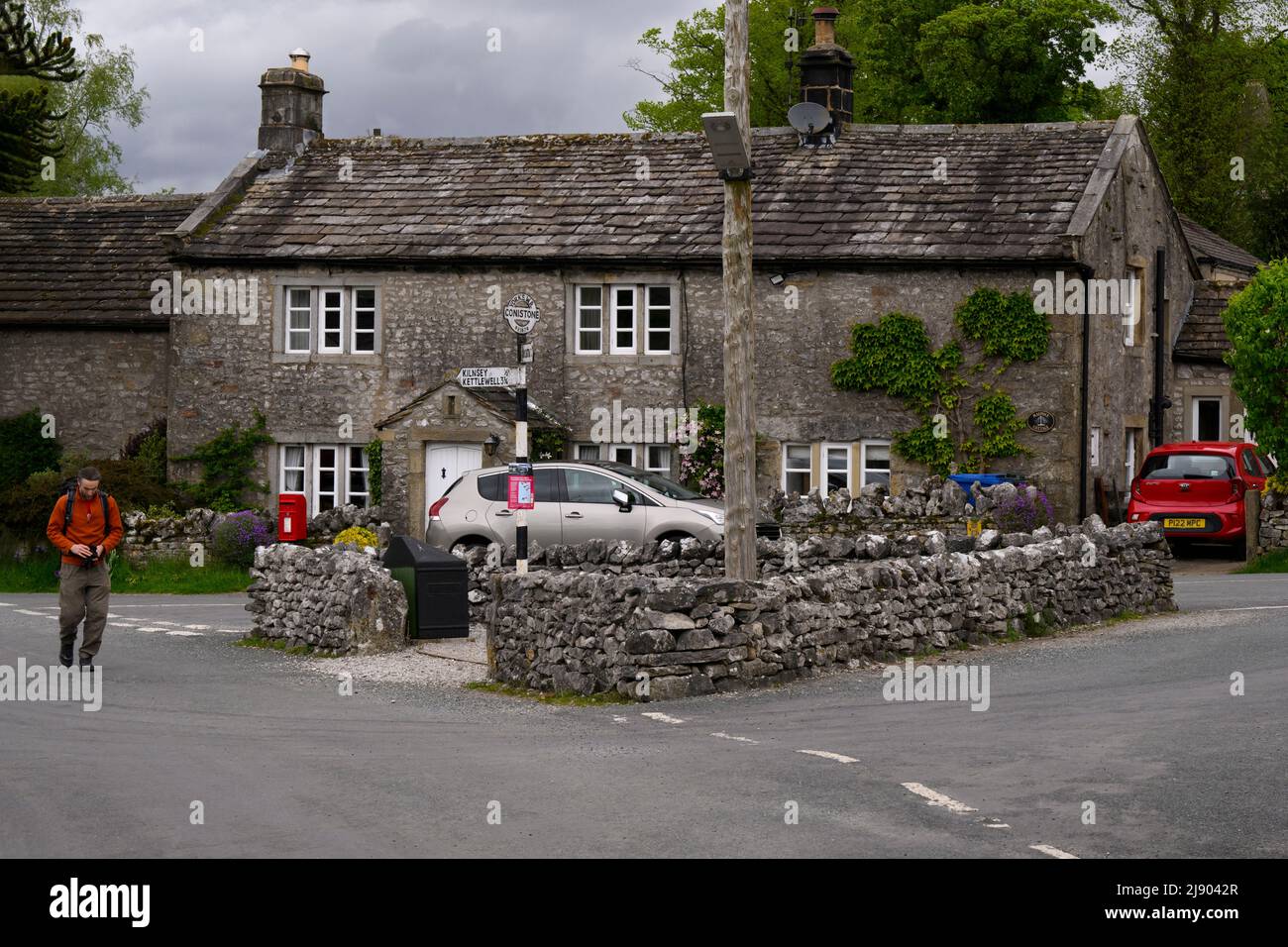 Conistone village centre (attractive stone properties, road junction, person walking, signpost pointing) - Wharfedale, Yorkshire Dales, England, UK. Stock Photo