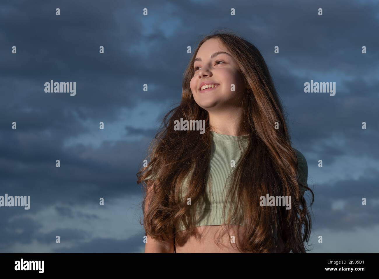 happy teen girl with long curly hair on sky background Stock Photo - Alamy