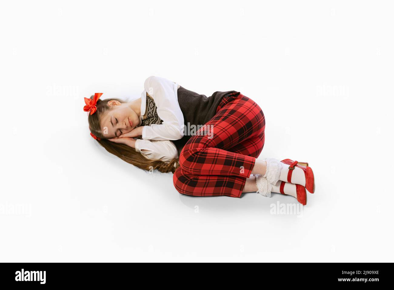 Portrait of beautiful young girl, teen in retro style clothes lying on floor with closed eyes on white studio background. Concept of art, beuty, youth Stock Photo