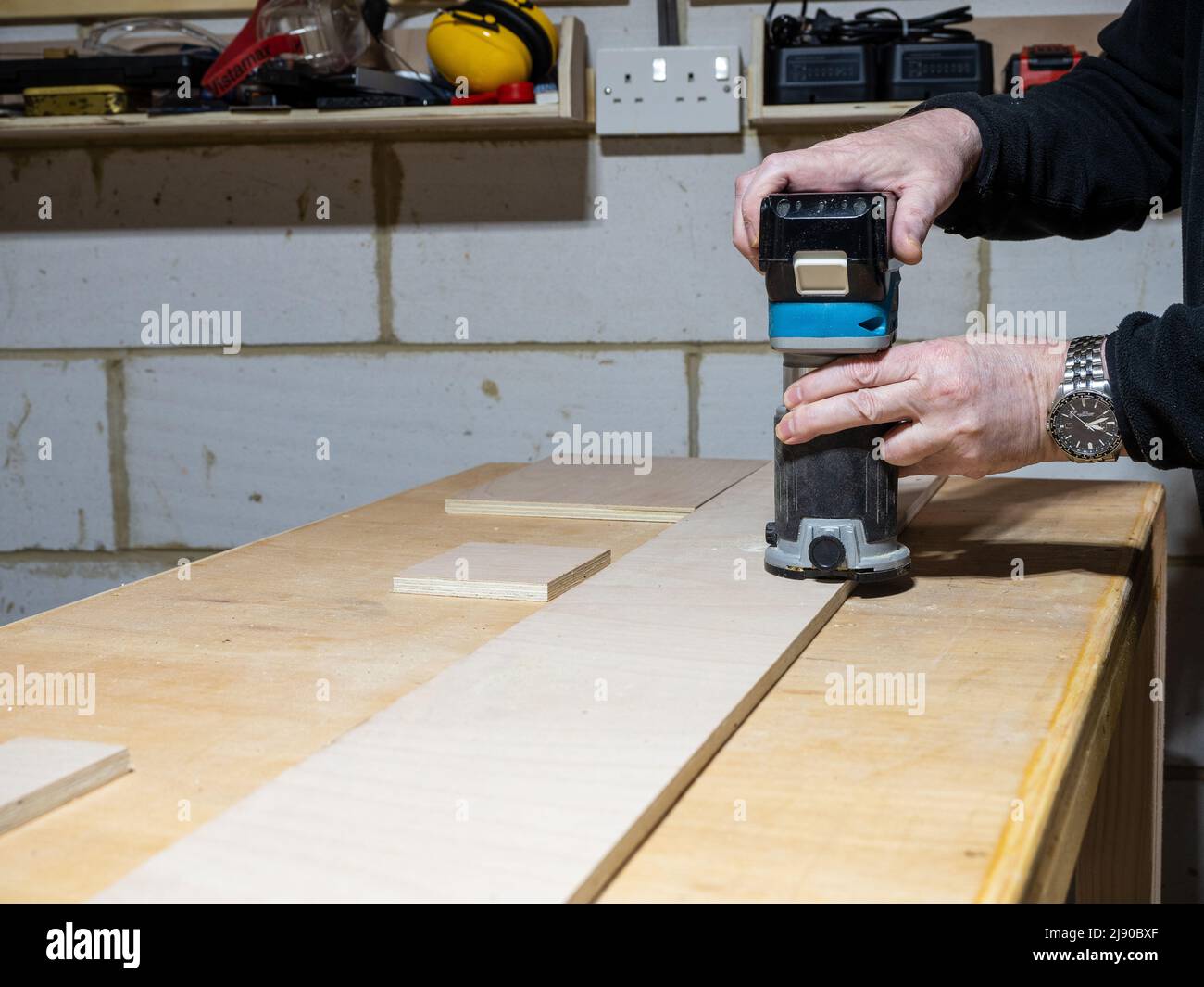 Carpenter operating a cordless battery powered trimming router to add a