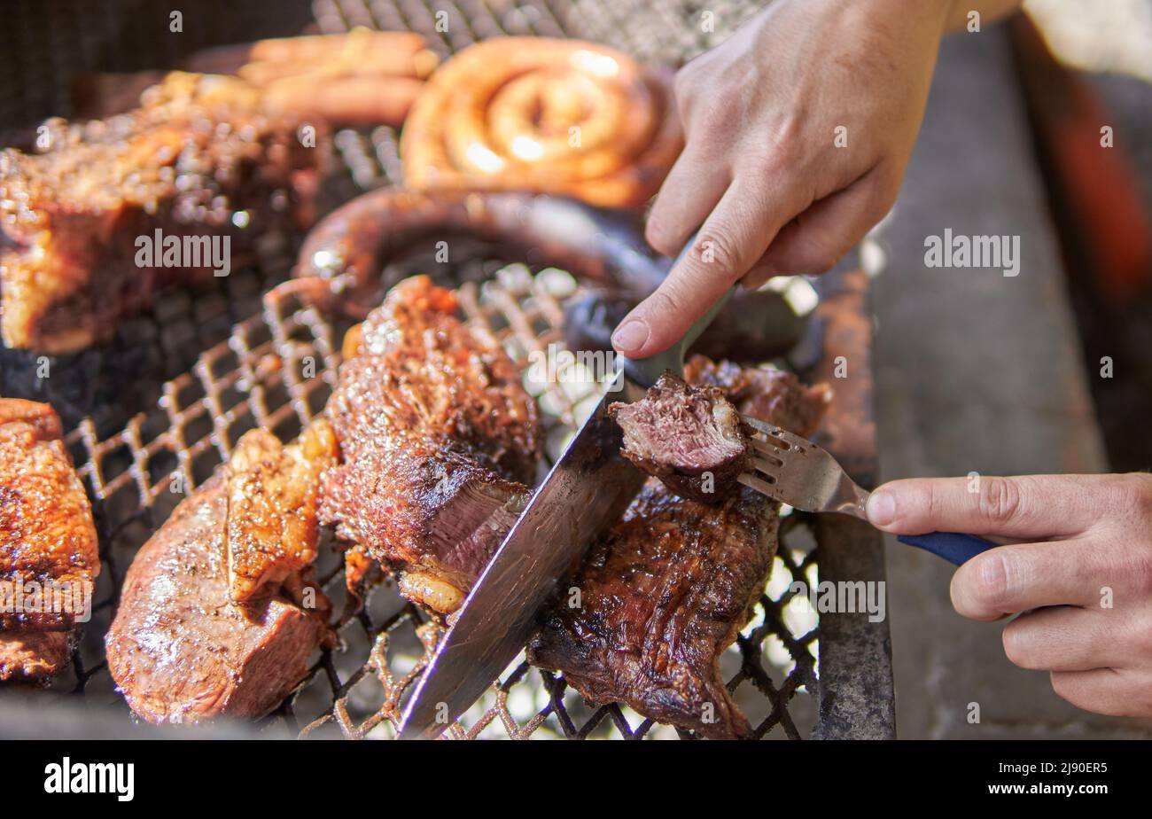 Man hands making barbecue for the lunch. Meat cuts, Coils of barbecued sausage and a blood sausage, beef on an iron grill. Traditional Argentinian bbq Stock Photo