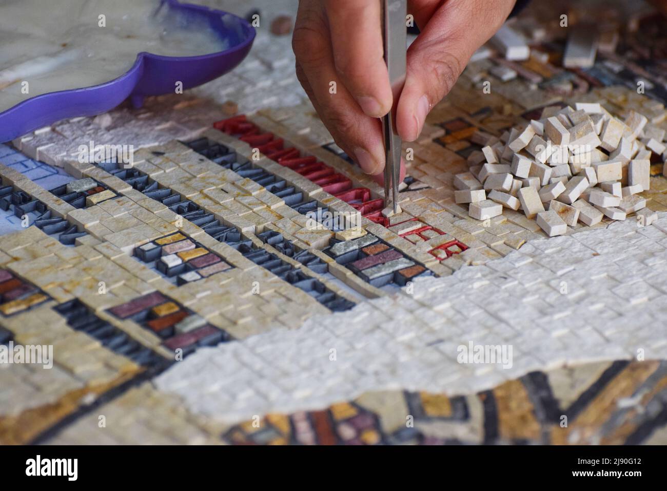 The hand of a Jordanian mosaic maker in action as she glues the tiny tiles in place with tweezers to make a piece of wall art Stock Photo