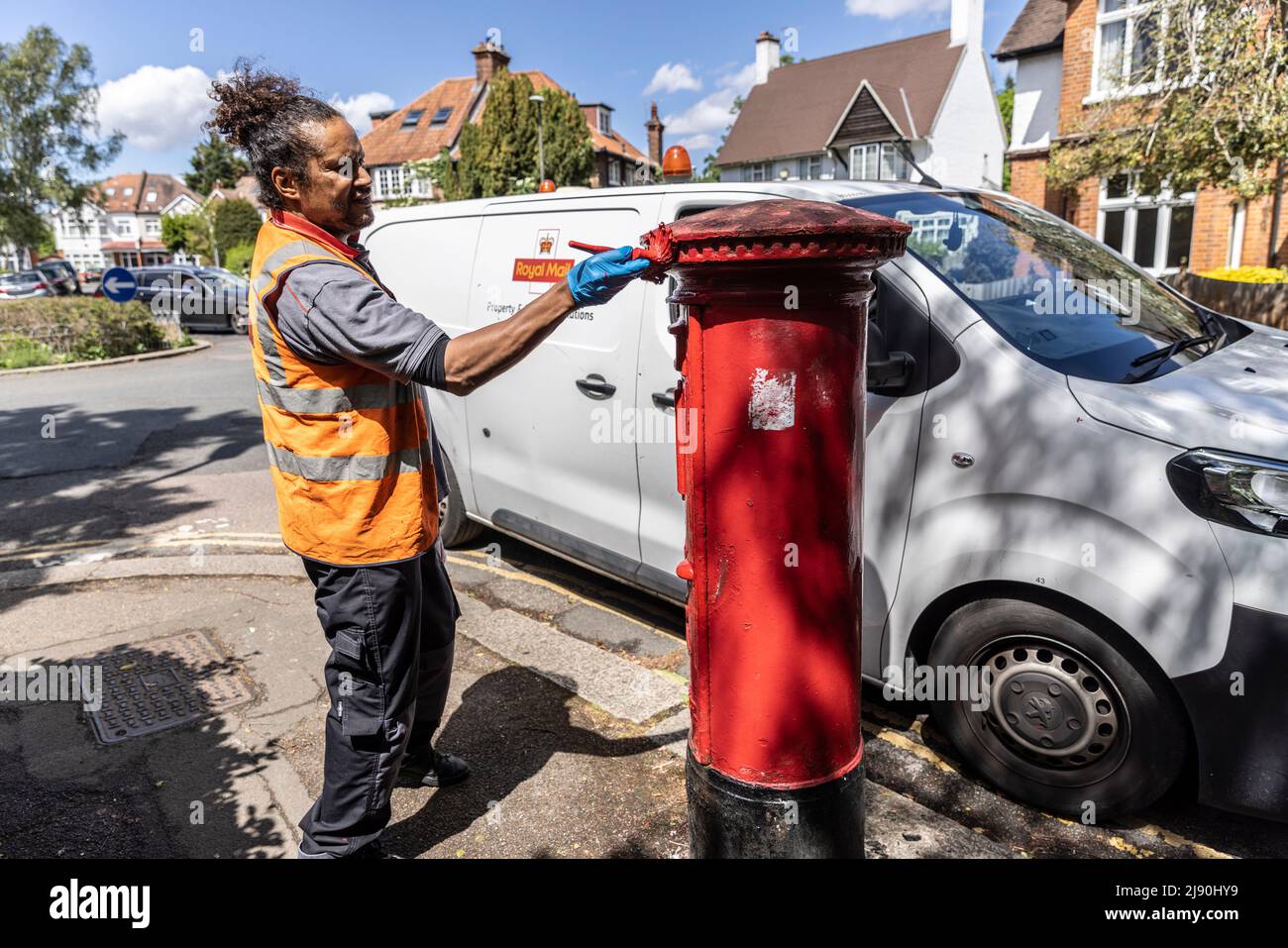 Royal Mail postal worker giving a post box a coat of red paint, London, England, UK Stock Photo