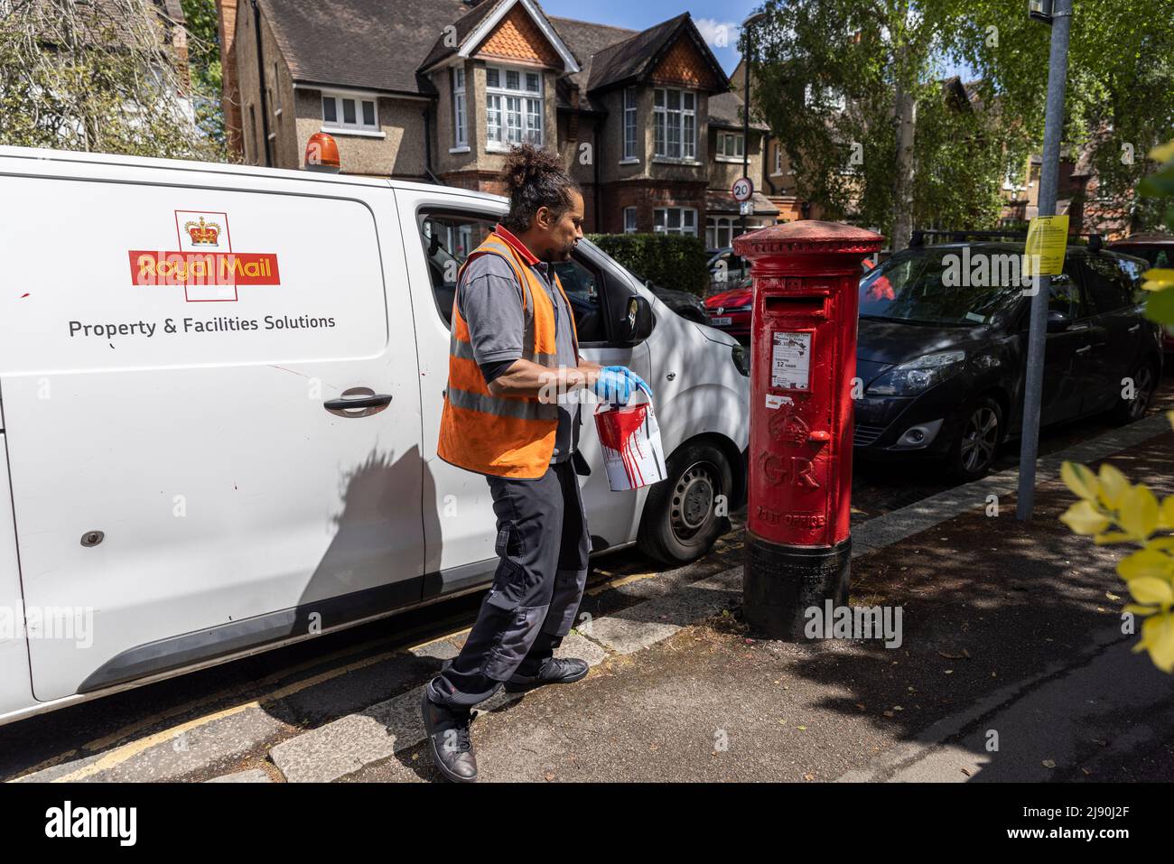 Royal Mail postal worker giving a post box a coat of red paint, London