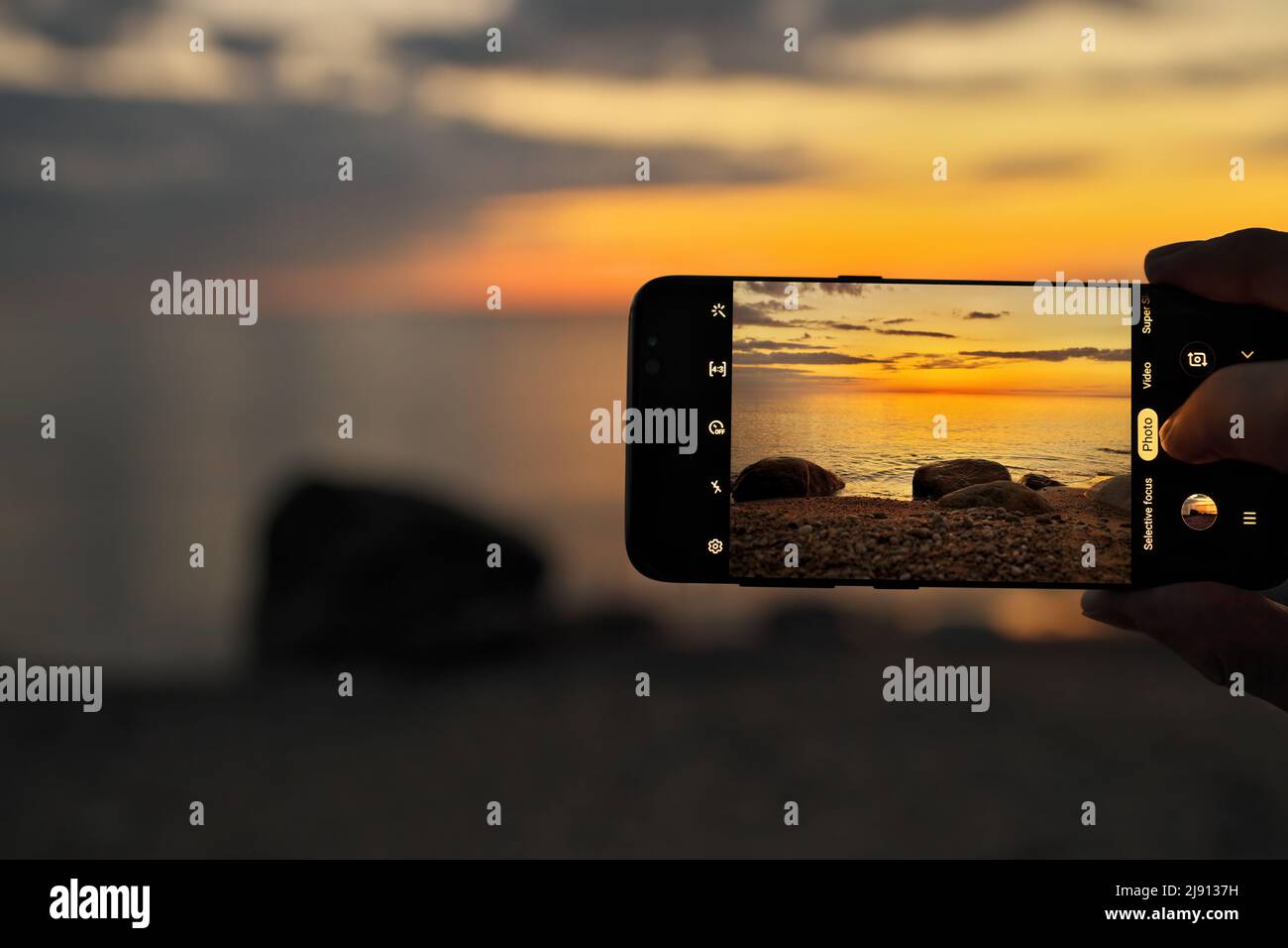 Close up of a hand holding and taking a mobile cell smart phone photo of a sunset beach scene photo Stock Photo