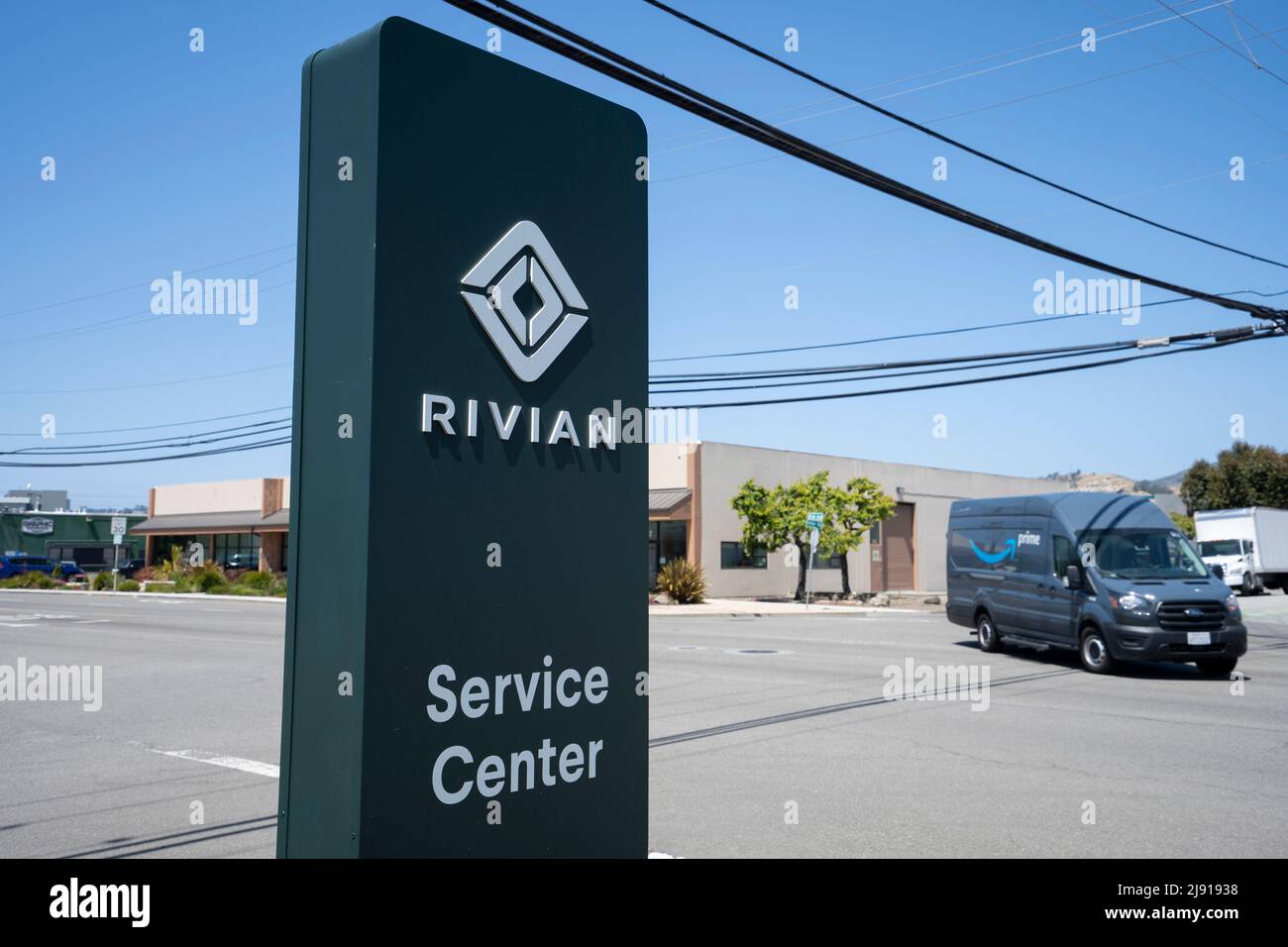 Rivian sign is seen at a Rivian service center, with an Amazon Prime branded Ford Transit van passing on the streets in the background, on May 1, 2022. Stock Photo